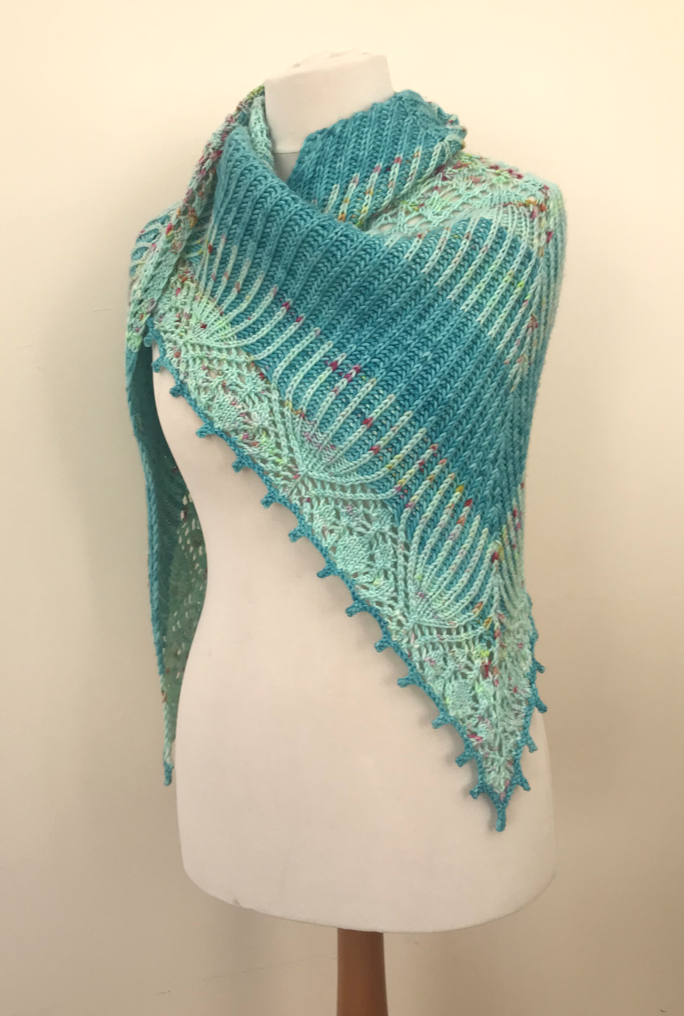 Triangular brioche and lace shawl draped over a mannequin so that the centre point is on the mannequin's left side, with the ends wrapped over the right shoulder.